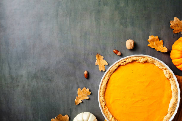 istock Top view of a pumpkin pie on a dark surface, surrounded by autumn leaves, nuts, and small pumpkins. Thanksgiving and fall-themed culinary concept. 2176235285
