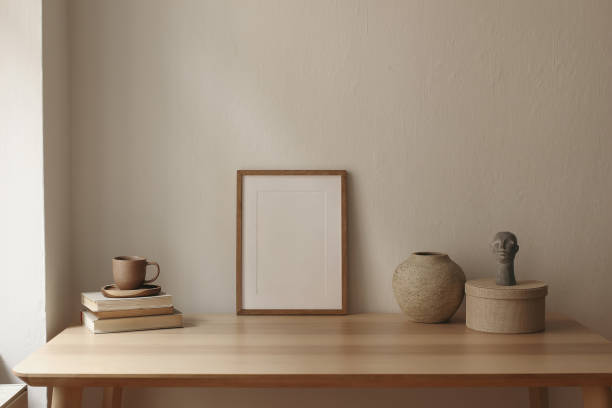 istock Artistic still life. Blank vertical picture frame mockup on wooden table. Scandi interior decor. Cup of tea, coffee, books. Boho busta sculpture, statue. Vase, round gift box. Beige wall background 2176240174