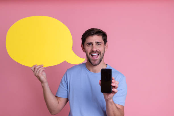 istock Excited man holding empty speech bubble and showing smartphone screen on pink background 2176247579
