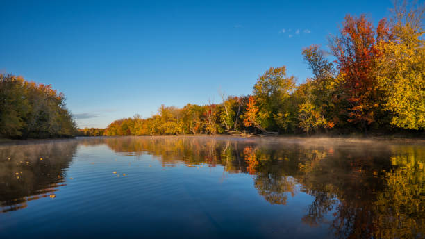 istock Autumn trees reflected in calm water with clear blue sky 2176256576