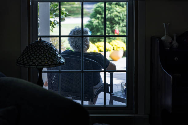 View looking through living room window at senior woman sitting outside relaxing on her home's front porch.