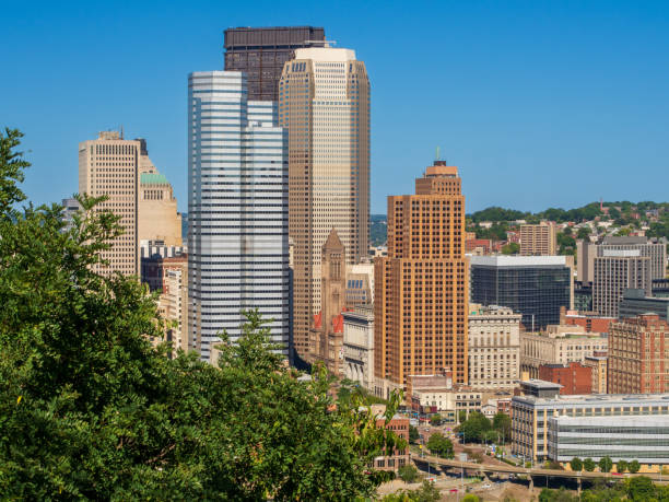 Downtown Pittsburgh, framed by green trees against clear blue sky. stock photo