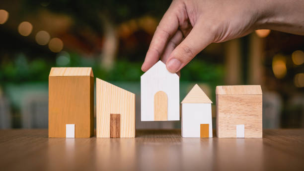 istock Hand choosing mini wood house model from model on wood table, selective focus, Planning to buy property. Choose what's the best. A symbol for construction ,ecology, loan concepts 2176290027