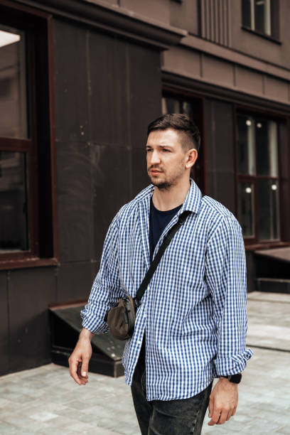 istock A man in a blue checkered shirt smiles while standing outside a modern building on a sunny day 2176329494