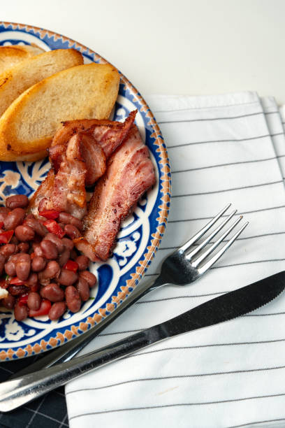 Delicious breakfast plate featuring eggs, beans, bacon, and potato wedges served on a decorative dish