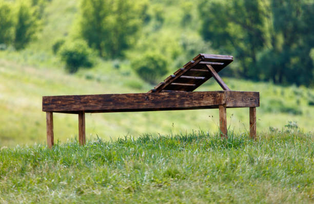 A wooden bench is sitting in a grassy field. The bench is open and has a wooden back. The field is lush and green, and the bench is the only object in the scene