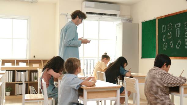 istock Smart teacher walking at classroom while looking at student homework. Pedagogy. 2176332615