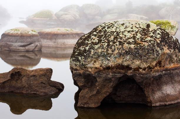 istock Foggy landscape with moss-covered rocks reflected in water 2176340046