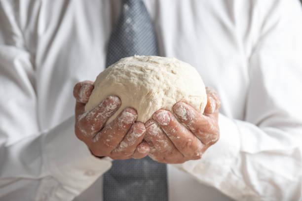 A close-up shot of a businessman holding a dough. The contrast between the formal attire and the act of dough preparation creates a symbolic image of balancing professional work with hands-on, creative tasks. This visual can represent entrepreneurship, hard work, and innovation in the business world, merging traditional craftsmanship with modern business practices.
