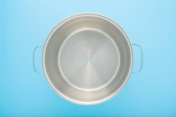 Empty new stainless cooking pot on light blue table background. Closeup. Pastel color. Top down view.
