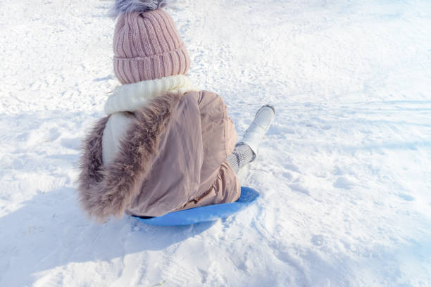 A young child slides down a snowy slope on a bright winter day.