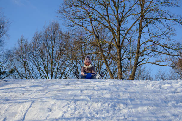 Two smiling children sledding down a snowy hill in a picturesque winter wonderland, relishing the thrill of speed and the joy of playing together in the crisp, cold air