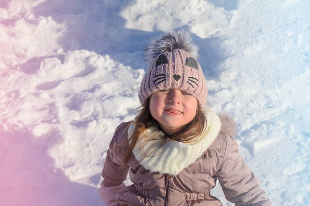 A child smiles while sitting in freshly fallen snow during a bright winter afternoon.