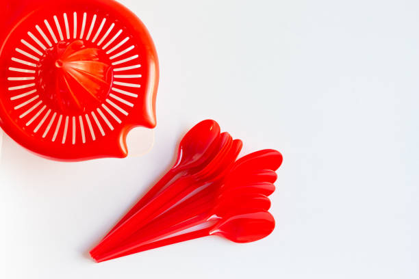 Spain. Top view of a red squeezer and red plastic spoons on a white table.