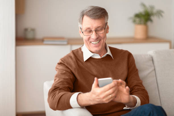 istock Positive Senior Gentleman Using Phone Sitting On Couch At Home 2176353050