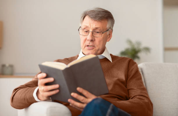 istock Retired man reading book sitting on couch at home 2176353090
