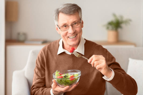 istock Senior Man Eating Vegetable Salad Sitting On Couch At Home 2176353103