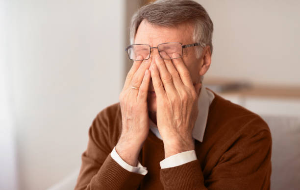 istock Senior Man Massaging Tired Eyes Sitting On Couch At Home 2176353120