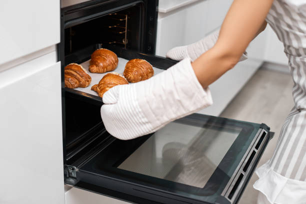 female baker taking tray with fresh croissants from oven in modern kitchen, close-up