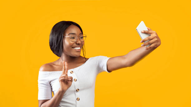 istock Afro Girl Making Selfie On Smartphone Gesturing V-Sign, Orange Background 2176355743