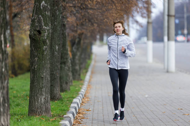 istock Woman Running Along Tree-Lined Pathway in Early Morning Fog 2176365342