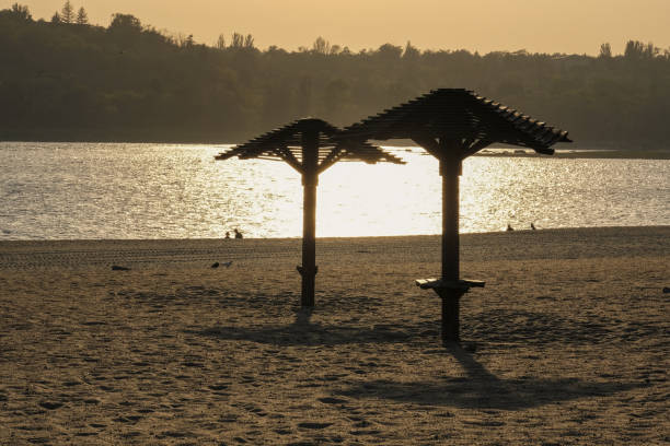 A beautiful, serene beach scene showcasing palm shade structures as the sun sets magnificently on the horizon