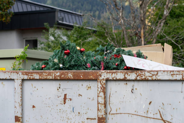 Discarded plastic fir trees decorated with red Christmas balls in a trash container