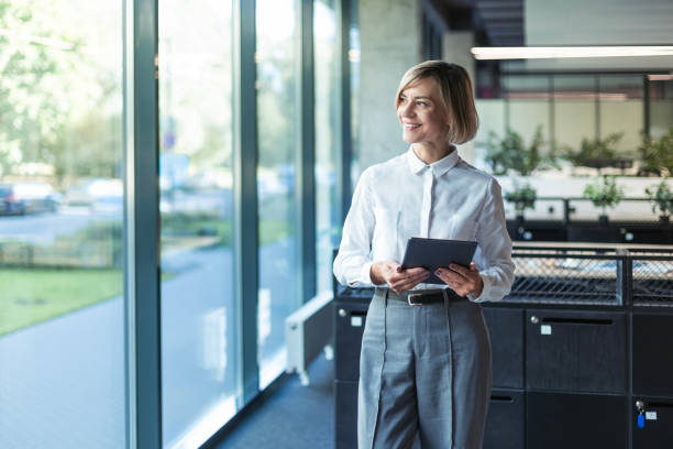 istock Smiling busy young businesswoman manager using tablet computer, executive looking out the window standing in office 2176388299