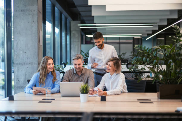 istock Four business professionals using laptop on desk discussing strategy company 2176391028