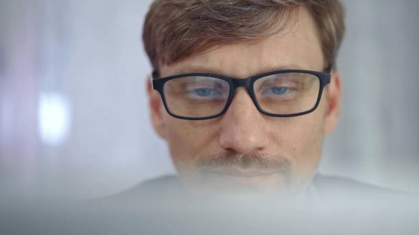 Businessman with glasses looking intently obscured partially by a translucent surface of laptop. Business concept.