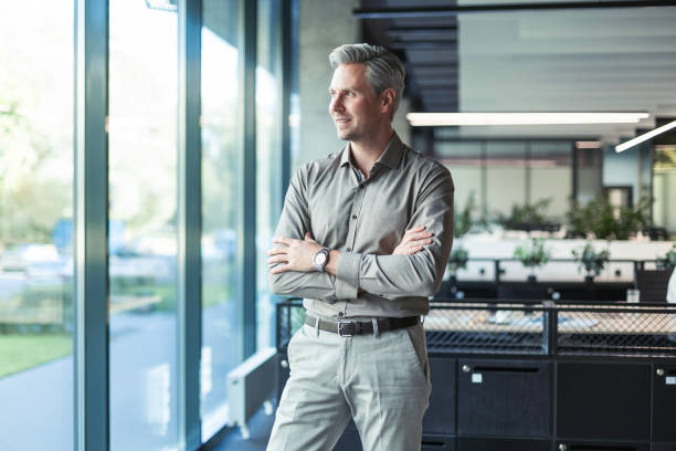istock Handsome successful businessman looking out the window hands crossed friendly chief standing at modern office indoors 2176392915