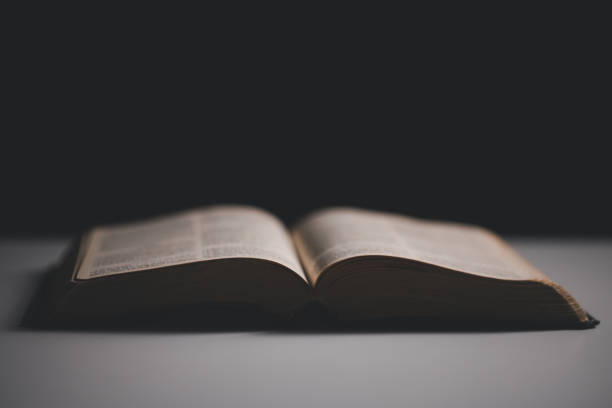 istock Old library, an open Bible lay on the table, its holy pages of scripture illuminated in the dark room. bible, holy, dark, old, open, library, pages, scripture, table, book, page. 2176394814