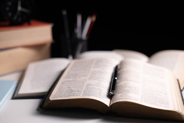 Old library, an open Bible lay on the table, its holy pages of scripture illuminated in the dark room. bible, holy, dark, old, open, library, pages, scripture, table, book, page.