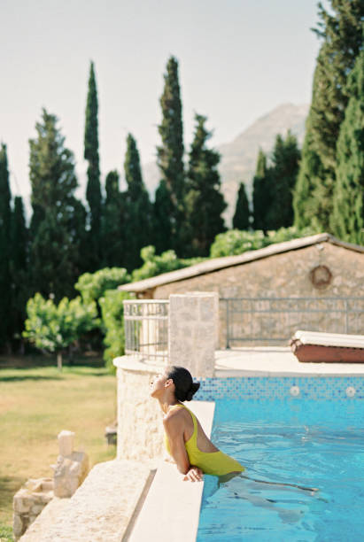 istock Young woman sunbathes while standing in the pool, leaning her elbows on the side. Side view 2176396564