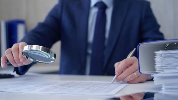 istock Businessman is carefully examining financial documents with a magnifying glass, highlighting the importance of thorough analysis in business. Audit and taxes 2176397318