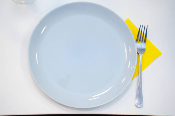 A simple dinner plate with a fork and a yellow napkin on the table. tableware for setting the table for every day and for holidays.