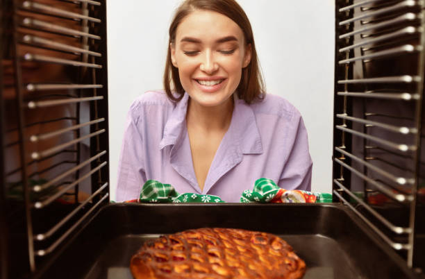 Cheerful millennial housewife taking tasty pie from oven
