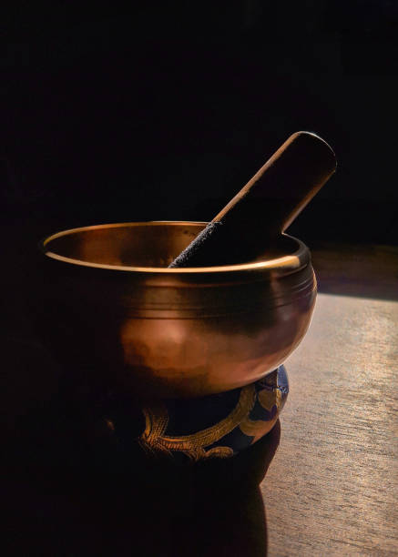 A close-up shot of a Tibetan singing bowl in soft natural light, casting deep shadows, highlighting its bronze tones and texture. A calming representation of meditation and peace