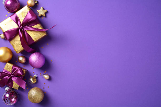 istock Merry Christmas greeting card design. Top view golden pattern gift boxes decorated purple ribbons, baubles, confetti on purple background. Flat lay. 2176409046