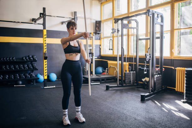 A young woman intensely focuses on her pole exercise in a modern gym, exemplifying her dedication to physical fitness and a healthy lifestyle amidst gym equipment.