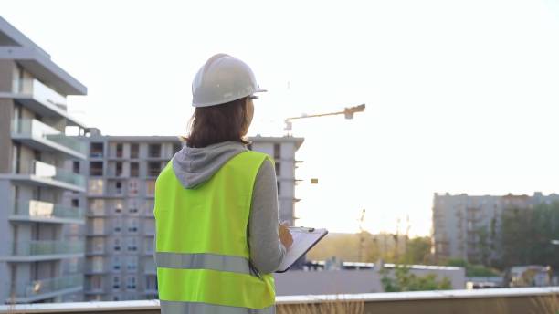 istock Female engineer with a white protective helmet and safety vest is writing on a clipboard while inspecting a construction site at sunset. Architect concept 2176425506