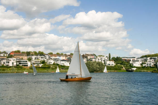 Wooden sail boat with white sails in a lake. Phoenix See, Dortmund, Germany. Residential houses in the background. Horizontal