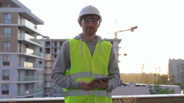istock Man construction site engineer holding tablet and wearing hard hat and safety vest with a sunrise at the background in early morning 2176432970