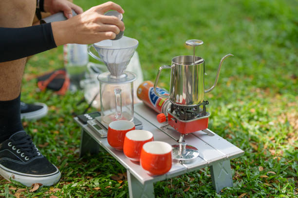 A cropped shot of a man making drip coffee on a picnic table while camping in a natural parkland in the morning.