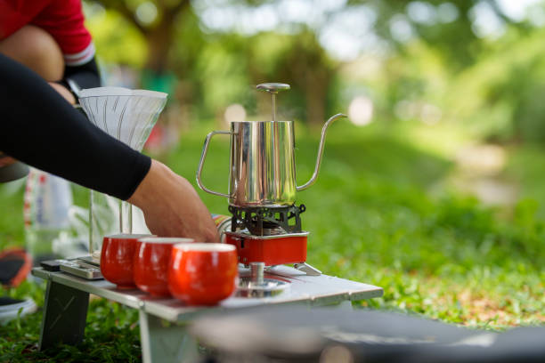 A cropped shot of a man making drip coffee on a picnic table while camping in a natural parkland in the morning.