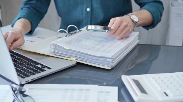 istock Businessman or professional auditor is analyzing data sheets. Close-up of an bookkeeper's hand with magnifying glass inspecting financial reports. Business audit and taxes 2176444112
