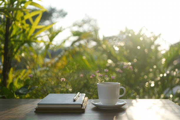 istock White coffee cup and notebook with lush green plant on wooden table under sunlight in the garden 2176452244