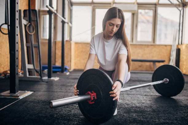istock Woman adjusts barbell on gym floor with focused effort. 2176453255