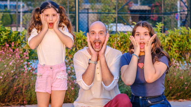 istock A middle-aged father looking at the camera with a surprised expression, alongside his daughters, in a wooded park on a late afternoon 2176453644