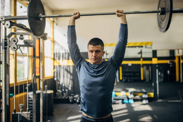 A person lifts a gray dumbbell with one hand against a textured wall for strength training.